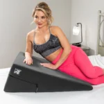 Beautiful woman in pink tights and black sports bra resting on the black Liberator Ramp Sex Pillow | Regular size 12"x24"x34"