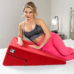 Beautiful woman in pink tights and black sports bra resting on the red Liberator Ramp Sex Pillow | Regular size 12"x24"x34"